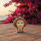 Handcrafted Teste di Moro ceramic head with crown, set against vibrant pink flowers and sunset.