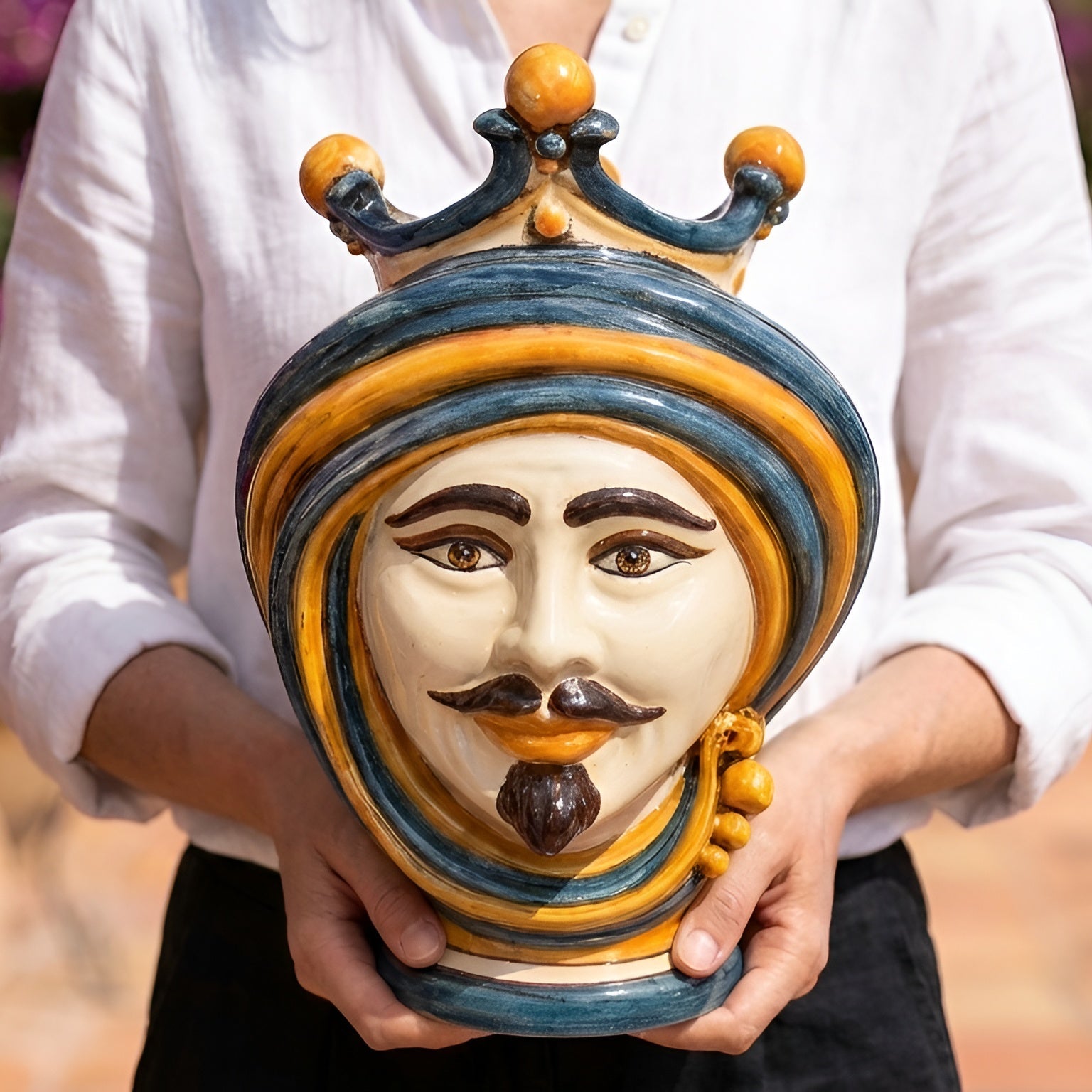 Handmade Testa di Moro ceramic vase with blue and gold crown, held by person in white shirt
