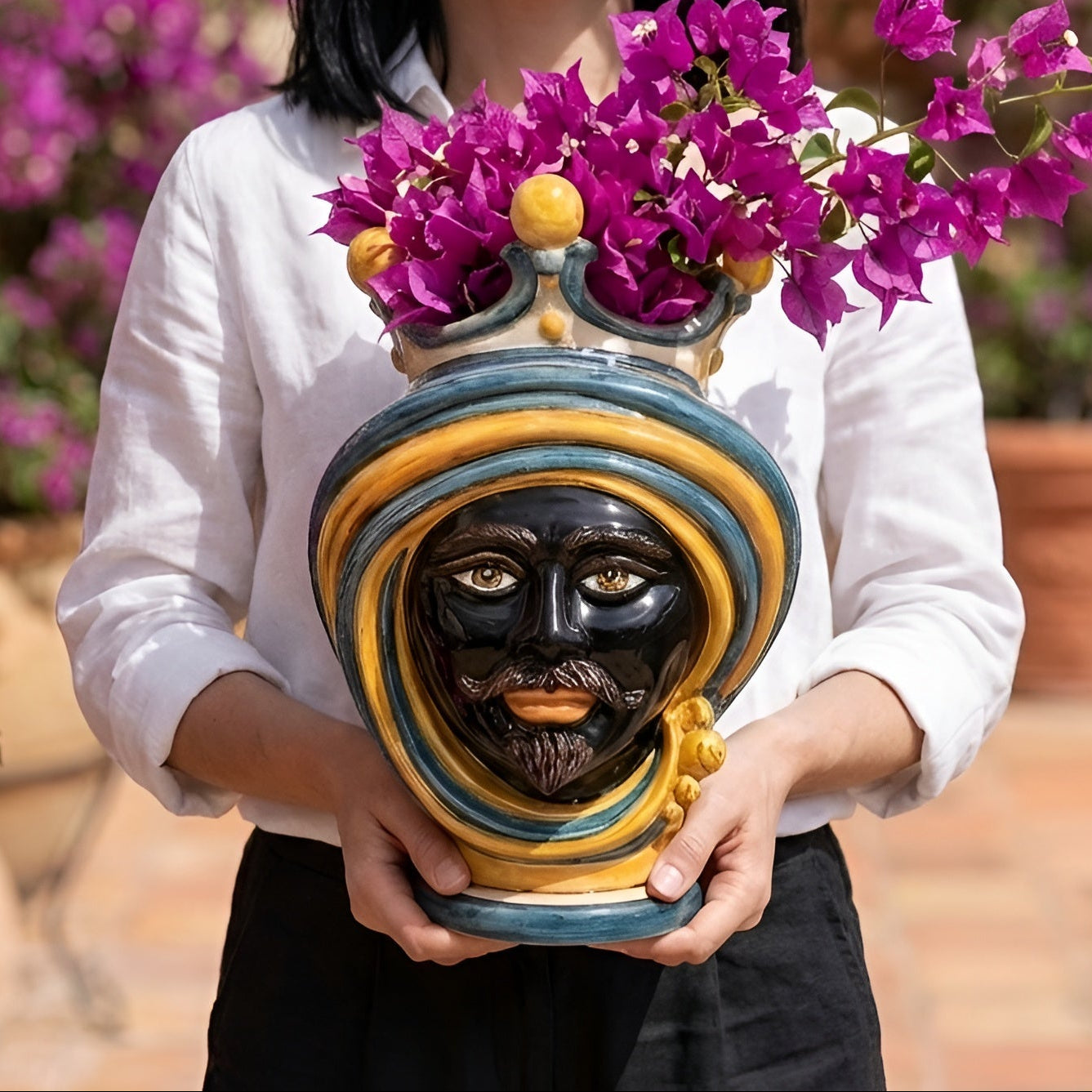 Handmade Teste di Moro vase with vibrant purple flowers, featuring traditional Sicilian design and bold colors.