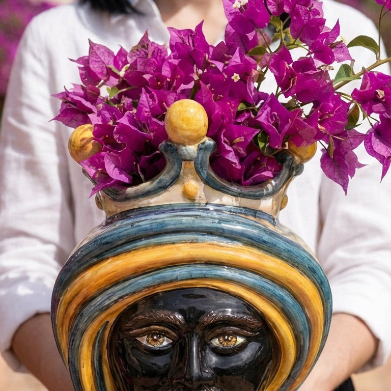 Handmade Teste di Moro vase with vibrant purple flowers, featuring bold blue and gold stripes and expressive eyes.