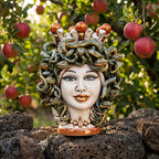 Handmade Medusa Testa di Moro ceramic sculpture with snake hair, set outdoors among apples and volcanic rocks.