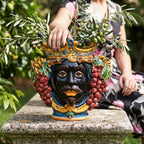 Hand-painted Teste di Moro vase with grape clusters, crown, and olive branches, styled outdoors on stone pedestal