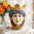 Hand-painted Sicilian Testa di Moro vase with crown, blue hair, and red beads, set against patterned tiles.