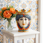 Hand-painted Teste di Moro ceramic vase with crown, displayed on white table beside orange peonies against patterned tile wall
