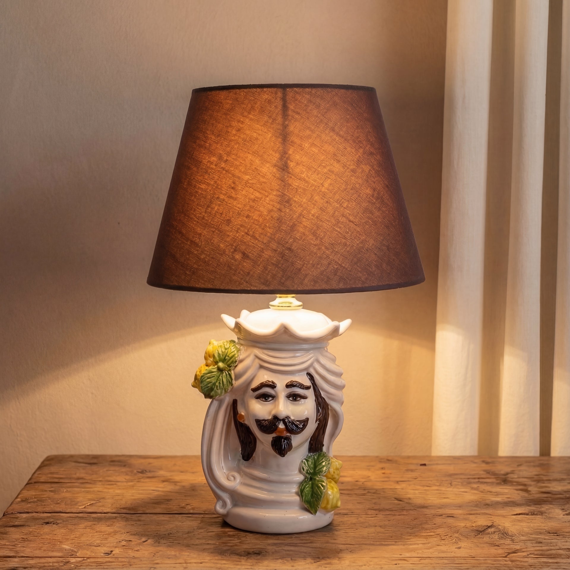 Handmade Teste di Moro table lamp with ceramic face, lemons, and brown shade on rustic wood.