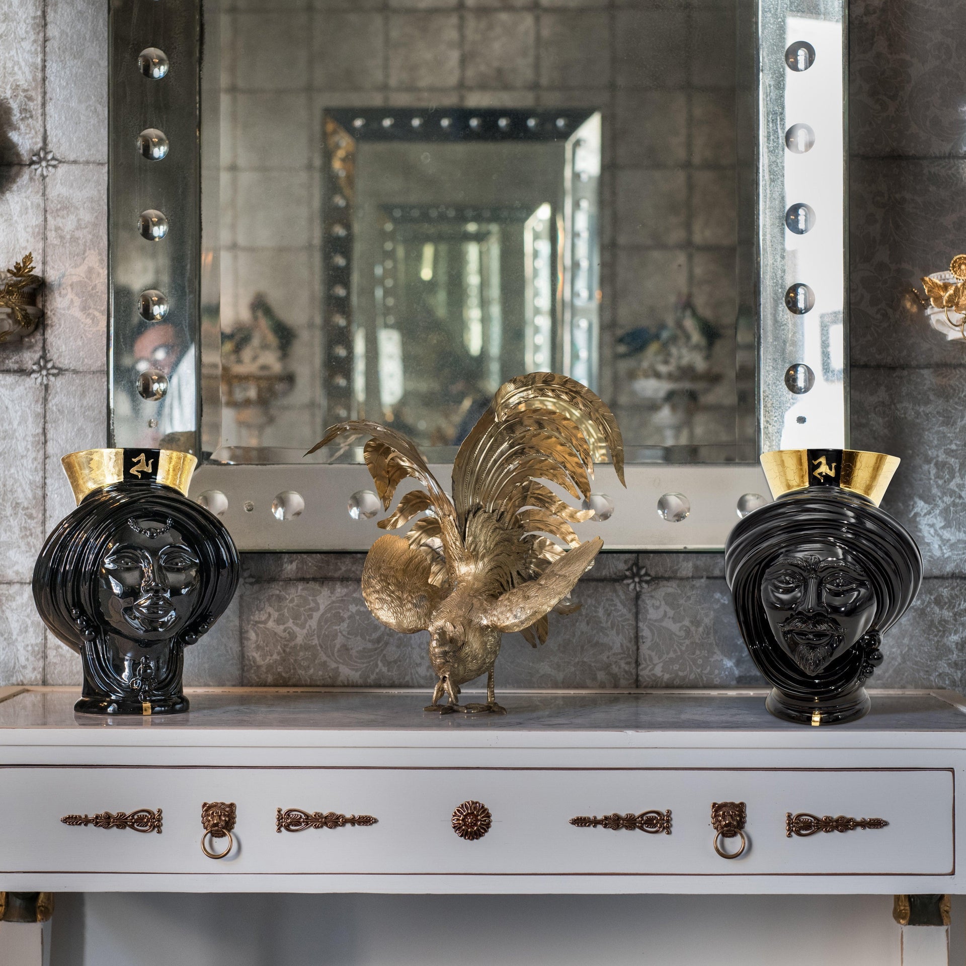 Black Teste di Moro vases with gold accents flanking a golden rooster sculpture on a console table