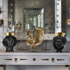 Black ceramic Teste di Moro vases with gold accents flanking a golden rooster sculpture on a console table