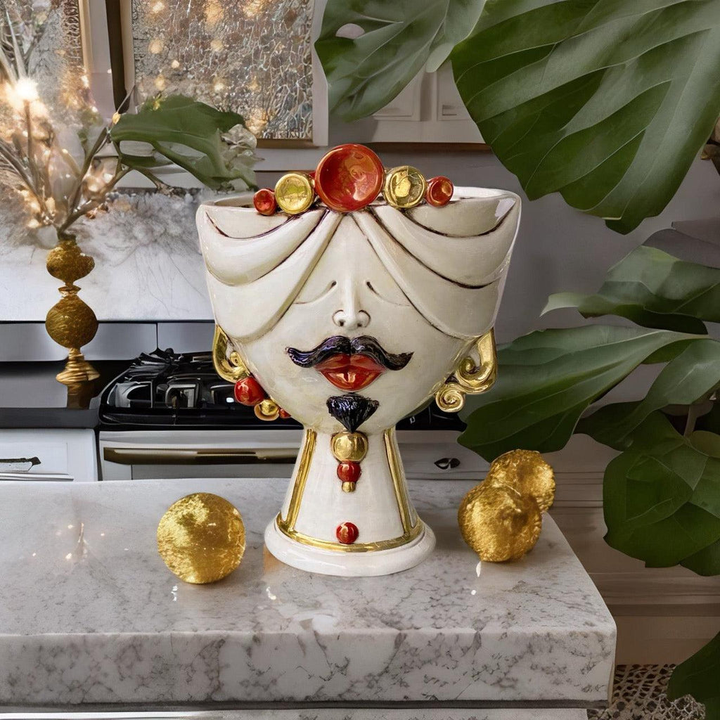 Handmade Teste di Moro ceramic vase with gold accents, red lips, and turban, displayed on marble countertop with green leaves.