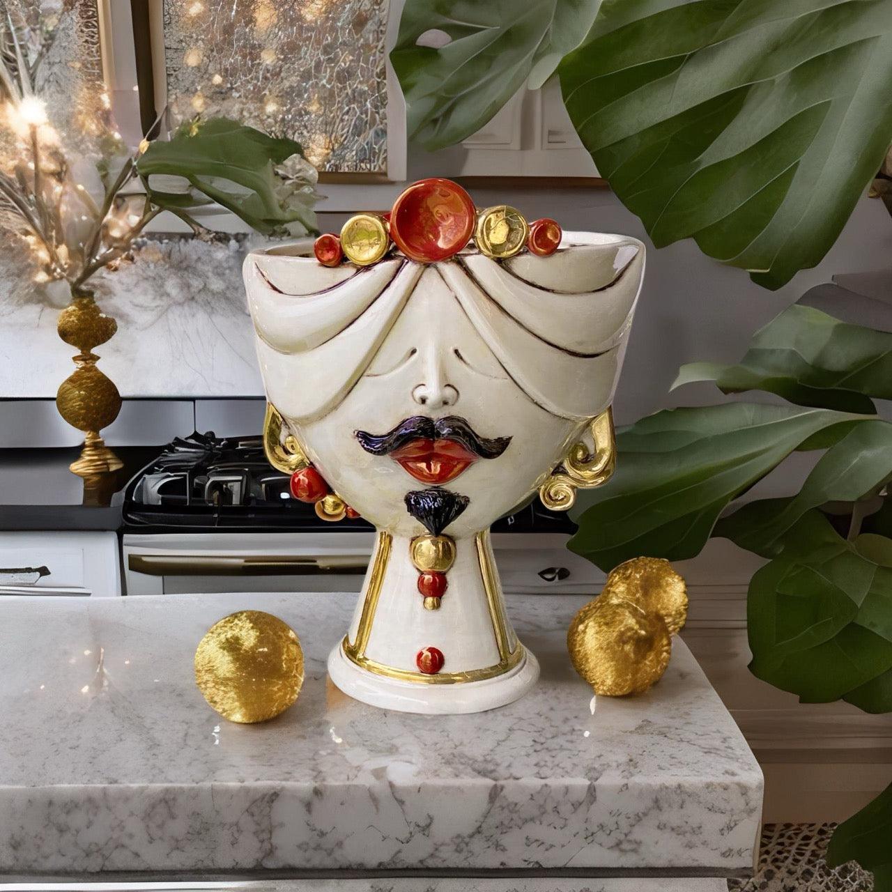 Handmade Teste di Moro ceramic vase with gold accents, red lips, and turban, displayed on marble countertop with green leaves.