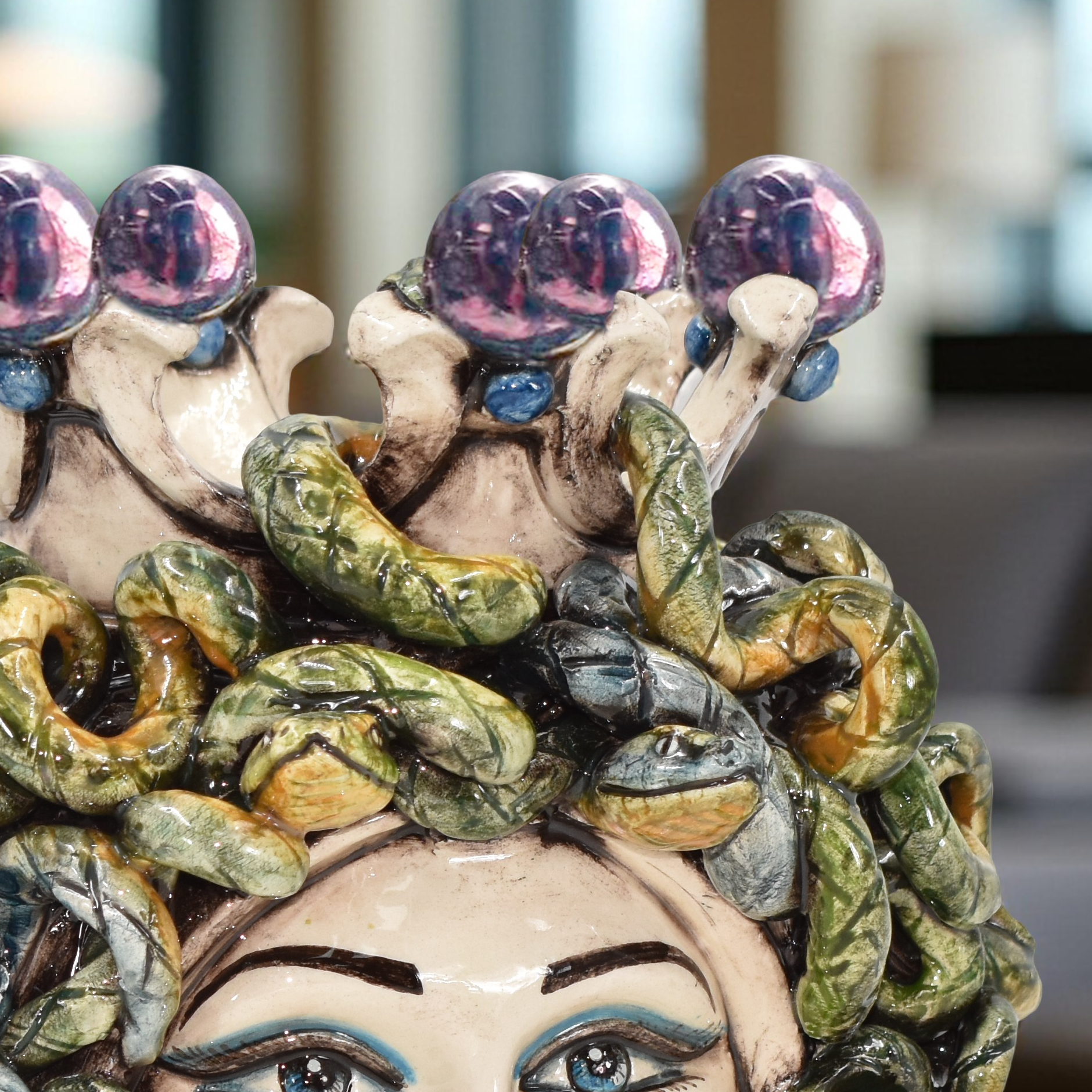 Handmade ceramic Medusa head with colorful snakes and purple flowers, blending tradition and modern design.