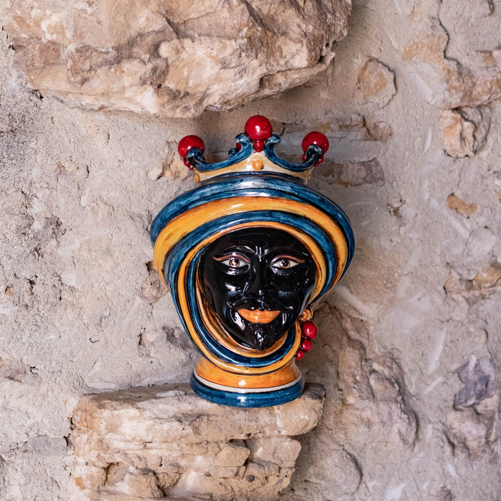 Handmade Teste di Moro ceramic wall decor with blue, gold, and red crown, displayed on rustic stone