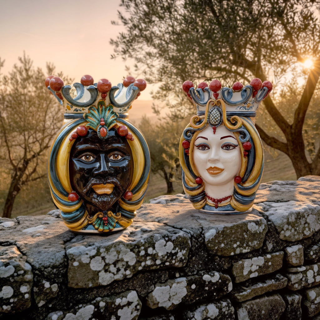 Handcrafted Teste di Moro ceramic statues, male and female, with ornate crowns, displayed on stone wall at sunset