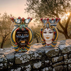Handcrafted Teste di Moro ceramic heads with vibrant crowns, displayed on stone wall at sunset