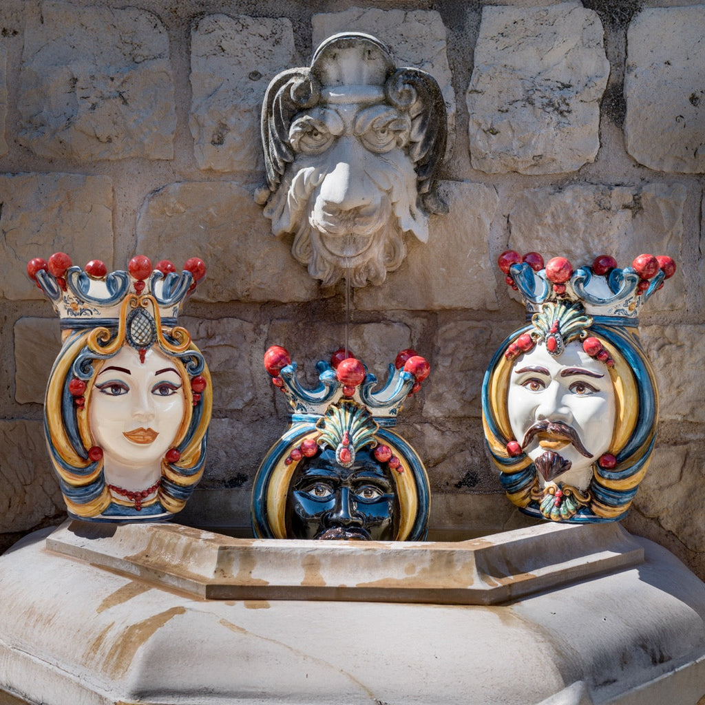 Handcrafted Teste di Moro fountain with colorful ceramic faces, traditional Sicilian design, stone wall backdrop