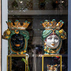 Handcrafted Teste di Moro ceramic vases with crowned faces, vibrant colors, and ornate details displayed in a shop window.