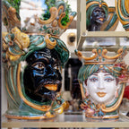 Handmade Teste di Moro ceramic vases with colorful crowns, green foliage, and detailed facial features, displayed in a shop window.